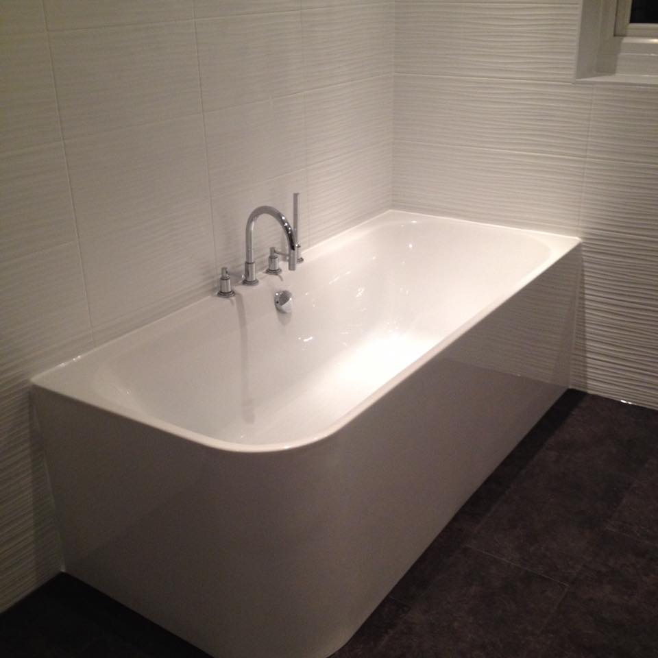 Freestanding bathtub installed against tiled wall